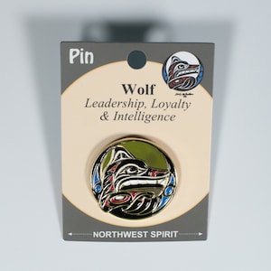 May include: A circular pin with a wolf design in black, red, and white, set against a green backdrop. The pin is displayed on a grey card with the word "Pin" and the text "Wolf Leadership, Loyalty & Intelligence".