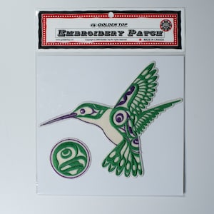 May include: Green and purple embroidered patch of a hummingbird with a circle design. The patch is on a white background with a red and white header that reads "Golden Top Embroidery Patch" and "Made in Canada".