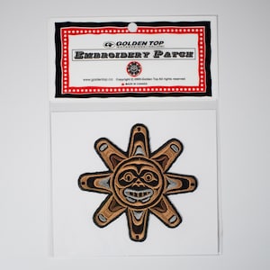 Peut inclure: Un écusson brodé brun et noir représentant un soleil stylisé avec un visage. L'écusson est dans un sac en plastique avec une étiquette rouge et noire qui indique "Golden Top Embroidery Patch".
