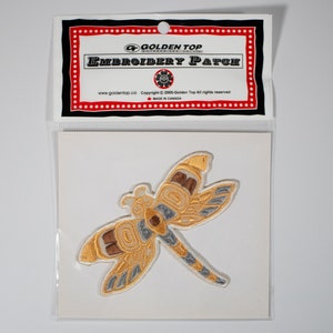 Könnte beinhalten: Ein goldfarbener gestickter Libellen-Patch mit braunen und grauen Akzenten. Der Patch ist in einer durchsichtigen Plastiktüte verpackt, auf der eine weiße Karte mit der Aufschrift "Golden Top Embroidery Patch" angebracht ist.