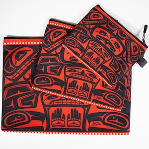 May include: Three red and black zippered pouches with a Native American design. The pouches are nested inside each other, with the largest pouch on the bottom and the smallest pouch on top. The design features a repeating pattern of stylized faces and hands.