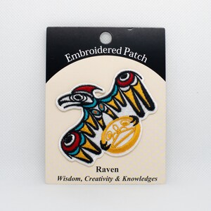 Puede incluir: Parche bordado con un cuervo colorido con un círculo amarillo. El texto "Embroidered Patch" está en la parte superior de la tarjeta y "Raven Wisdom, Creativity & Knowledges" está en la parte inferior.