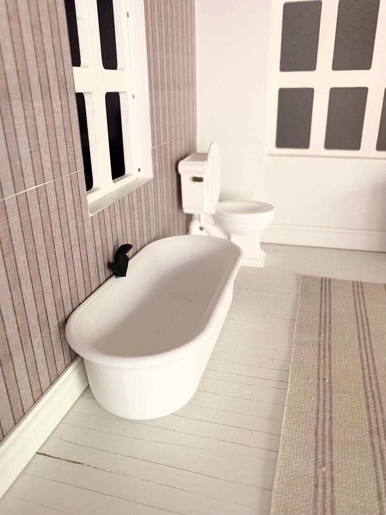 May include: A white bathtub with a black faucet in a dollhouse bathroom. The bathroom has white tile floors and a white toilet.