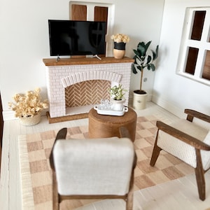 May include: Miniature living room scene with a fireplace, TV, and two armchairs. The fireplace is white brick with a wooden mantel. A small rug with a checkered pattern is on the floor. A small table holds a tray with glasses.
