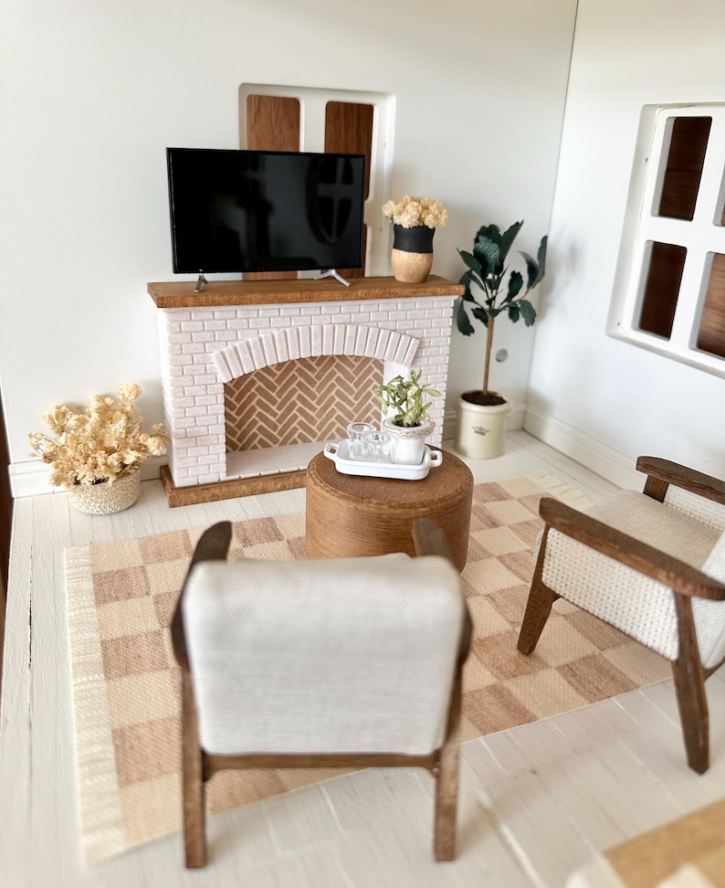 May include: Miniature living room scene with a fireplace, TV, and two armchairs. The fireplace is white brick with a wooden mantel. A small rug with a checkered pattern is on the floor. A small table holds a tray with glasses.