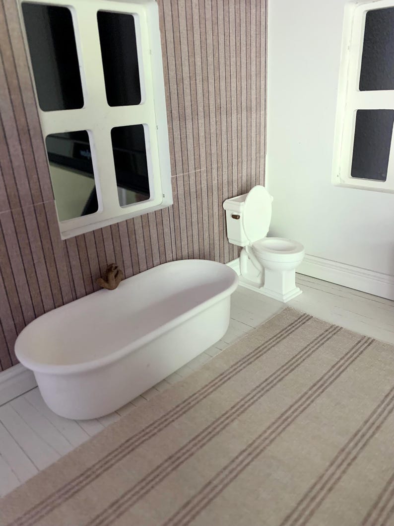 May include: A white bathtub with a brown faucet, a white toilet with a white seat, and a striped rug in a dollhouse bathroom.