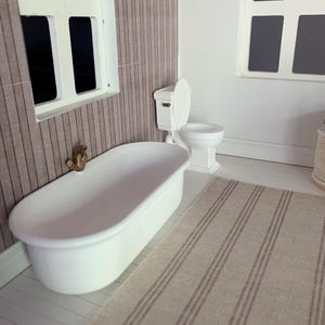 May include: A white bathtub with a gold faucet sits in a bathroom with a white toilet and a striped rug. The bathroom has wood paneling on the walls.