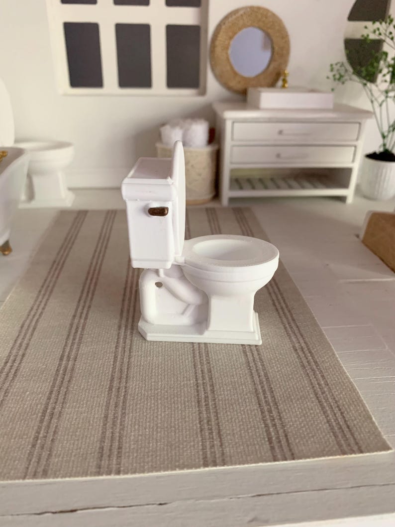 May include: White miniature toilet with a gold handle, sitting on a striped rug in a dollhouse bathroom.