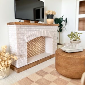 May include: Miniature living room scene with a white brick fireplace, a black TV, and a wooden coffee table. The fireplace has a herringbone pattern inside. A checkered rug and decorative plants complete the cozy interior.