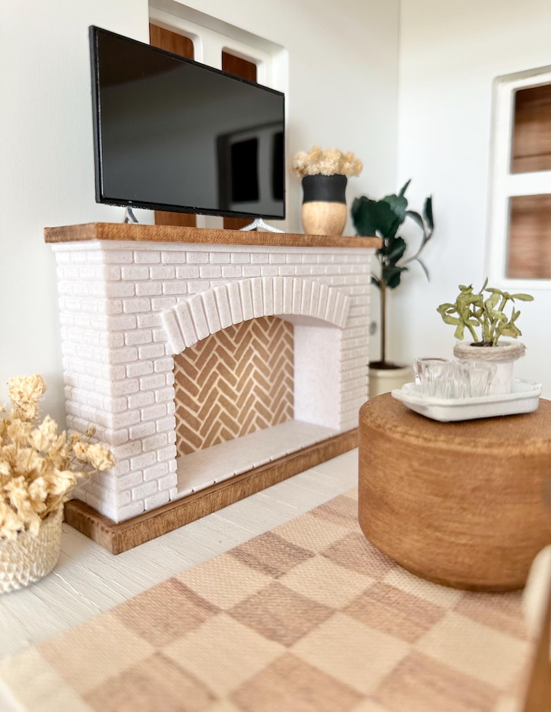 May include: Miniature living room scene with a white brick fireplace, a black TV, and a wooden coffee table. The fireplace has a herringbone pattern inside. A checkered rug and decorative plants complete the cozy interior.