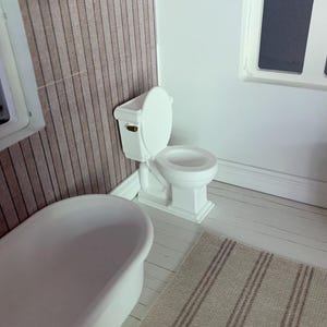 May include: A white toilet with a white bathtub in the background. The toilet has a white seat and a white tank. The bathroom has a white floor and a brown striped rug.