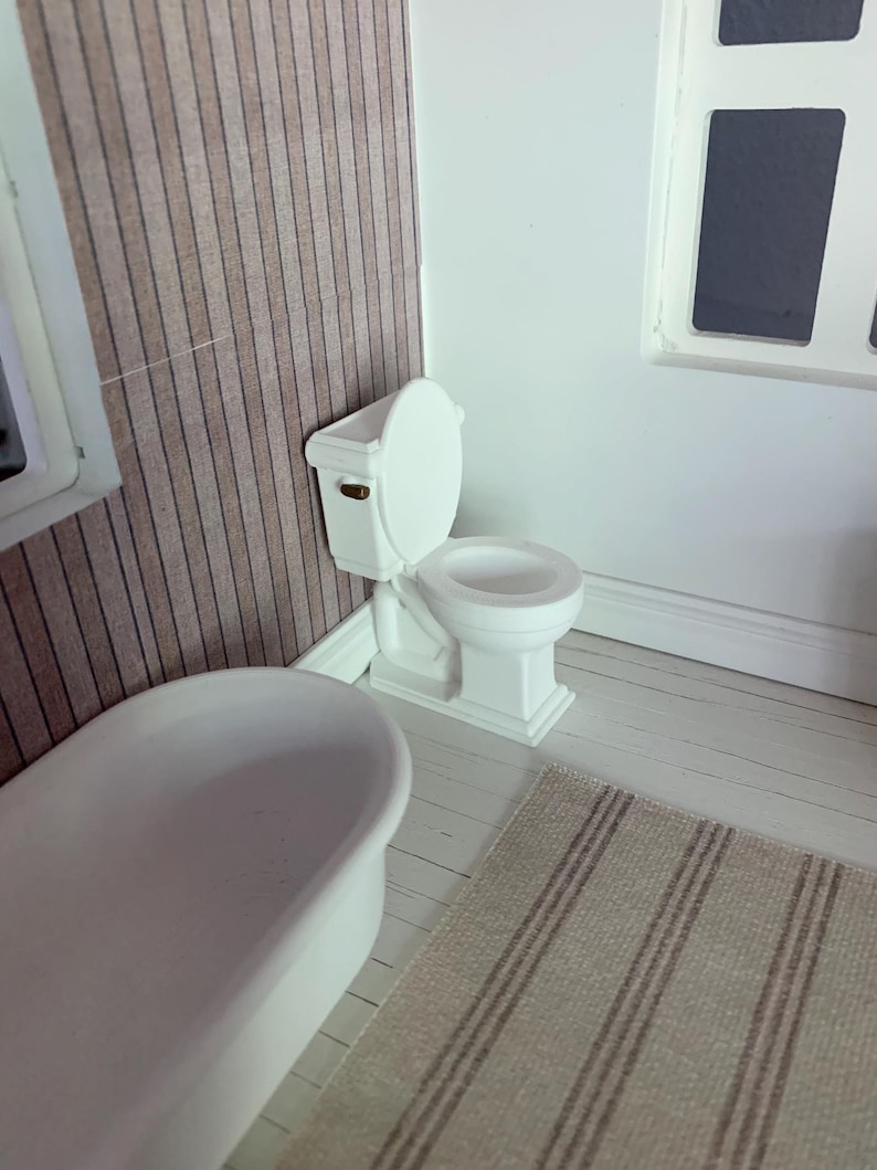 May include: A white toilet with a white bathtub in the background. The toilet has a white seat and a white tank. The bathroom has a white floor and a brown striped rug.