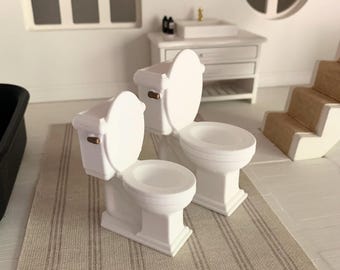 May include: Two white miniature toilets with gold accents on a striped beige rug. The toilets are in a dollhouse bathroom setting.