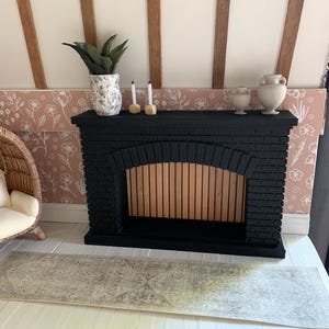 May include: A black brick fireplace with a wooden mantel and a wood-burning insert. There are two white candles and a potted plant on the mantel.