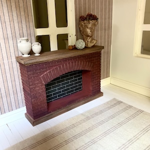 May include: A miniature brick fireplace with a black hearth and a wooden mantel. Two white ceramic urns are on the mantel, along with a gold bust with a floral crown. A beige and brown striped rug is in front of the fireplace.
