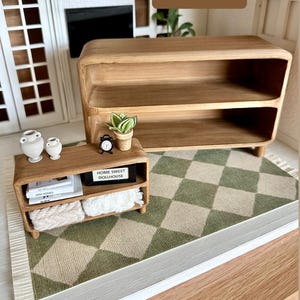 May include: Miniature wooden furniture set, including a two-shelf cabinet and a smaller table, displayed on a green and white checkered rug. The set includes decorative items like vases, a clock, and a potted plant. The text "HOME SWEET DOLLHOUSE" is visible.