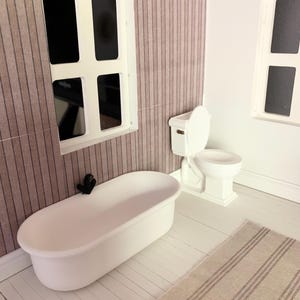 May include: A white bathtub and toilet in a dollhouse bathroom with a striped wallpaper and white wood floor. The bathroom also has a white rug with brown stripes.