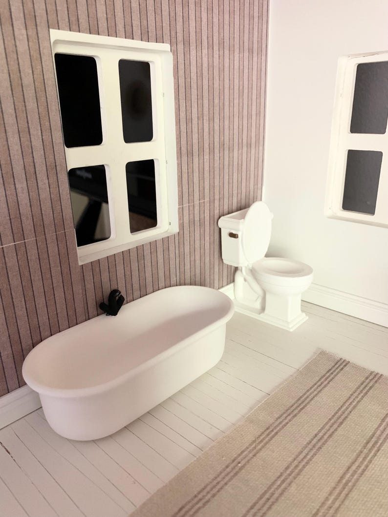 May include: A white bathtub and toilet in a dollhouse bathroom with a striped wallpaper and white wood floor. The bathroom also has a white rug with brown stripes.