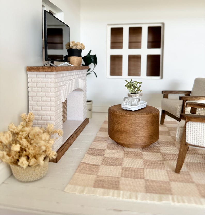 May include: Miniature living room scene with a white brick fireplace, a TV, and a brown wooden coffee table. A checkered rug in shades of beige and brown sits on the floor. The scene includes a window, a chair, and decorative plants.