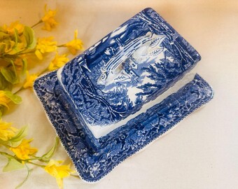 May include: A blue and white ceramic butter dish with a lid featuring a floral design. The lid has a handle in the shape of a leaf.