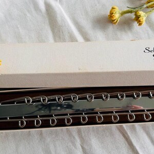 May include: A vintage tie rack with a wooden base and a silver metal bar with hooks. The box reads "Selecto Deluxe Tie Rack Made in U.S.A."