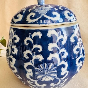 May include: A blue and white ceramic jar with a lid. The jar features a floral and scroll design. The lid has a small handle. The jar is a decorative piece.