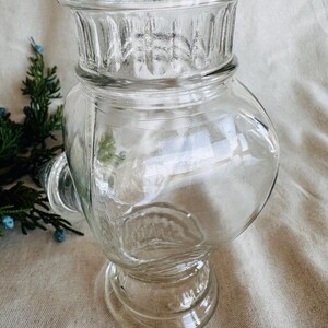 May include: A clear glass jar with a wide mouth and a textured design. The jar has a round base and a short neck.