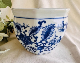 May include: A white ceramic planter with a blue floral pattern. The planter has a hexagonal shape and a slightly flared rim. The blue design features stylized flowers and leaves. The planter is suitable for small plants or succulents.
