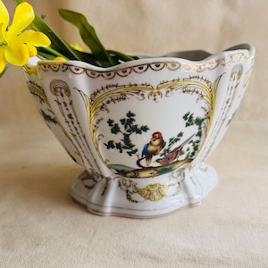 May include: A white ceramic mug with a black handle and the text "But First, Coffee" in a bold, black font. The mug is set against a blurred background, suggesting a cozy setting. The mug appears to be approximately 4 inches tall.