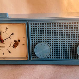 May include: Vintage blue RCA clock radio. The clock face is white with black hands and markers, and the word "RCA" is printed at the bottom. The radio section has a grid design with two blue knobs. A retro home decor item.