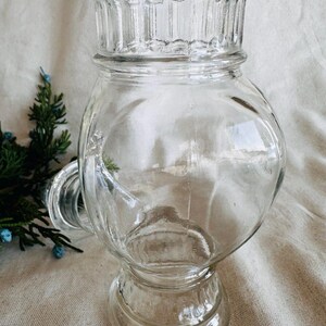 May include: A clear glass jar with a wide mouth and a decorative base. The jar has a fluted rim and a rounded body.