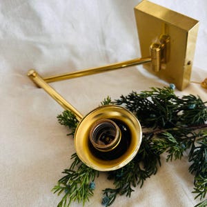 May include: A gold-toned wall-mounted light fixture with a single bulb socket and an adjustable arm. The fixture is mounted on a square base and has a simple, modern design.