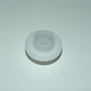 Puede incluir: Pequeño objeto de plástico blanco con base circular y parte superior cilíndrica. El objeto parece ser un tapón, probablemente para una botella o recipiente. El material es translúcido y el diseño es simple y funcional.