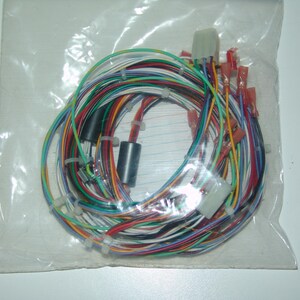 May include: A coiled electrical wiring harness featuring multiple thin wires in various colors including red, green, blue, white, and black. The bundle is secured with white plastic zip ties and includes two white plastic connectors and several red crimp terminals.