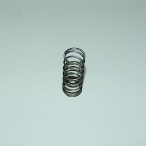 May include: A close-up of a metallic silver compression spring. The spring is cylindrical, with multiple coils stacked on top of each other. The spring is made of a shiny, reflective metal.