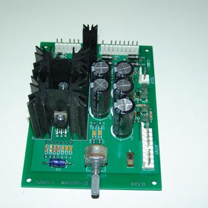 Può includere: Una scheda di circuito stampato verde con componenti neri, tra cui un dissipatore di calore, condensatori e un potenziometro. La scheda ha la scritta "AUDIO II A043681-U2 REV D" stampata su di essa.