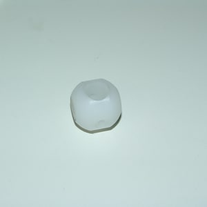 Puede incluir: Una pequeña cuenta de plástico blanco y redondeada con un agujero cilíndrico en el centro. La cuenta tiene una forma ligeramente irregular con algunas pequeñas hendiduras en su superficie. Sobre un fondo blanco.