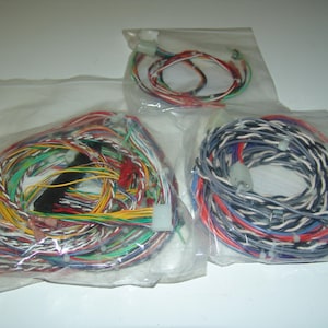 Puede incluir: Tres paquetes de cables eléctricos de colores en bolsas de plástico transparente. Los cables son de varios colores, incluyendo rojo, verde, amarillo y azul. Cada paquete tiene un conector en el extremo. Los cables están enrollados y parecen nuevos.
