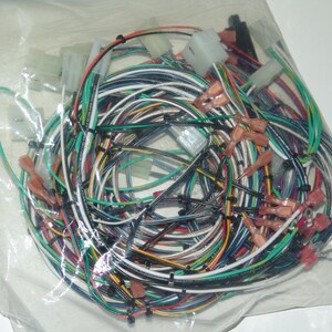 Puede incluir: Un conjunto de cables eléctricos multicolores, incluyendo negro, blanco, verde y amarillo, con varios conectores y terminales. Los cables están contenidos en una bolsa de plástico transparente, lo que sugiere que son nuevos y listos para usar.