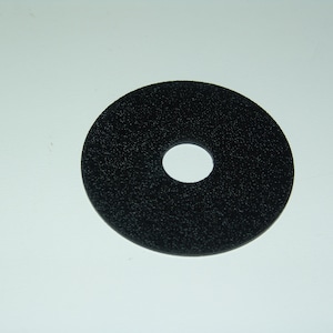 May include: A black, circular abrasive disc with a central hole. The disc has a textured surface, likely for grinding or polishing. The object is set against a plain white background.