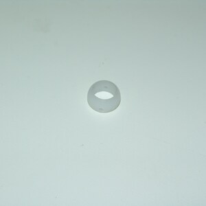 Puede incluir: Un pequeño objeto translúcido en forma de anillo. El anillo es de color blanco roto pálido y parece estar hecho de un material liso, posiblemente plástico. Tiene un agujero circular en el centro.