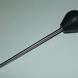 May include: A black, teardrop-shaped knob attached to a long, silver metal rod. The rod is cylindrical and has a small hole at the end. The object is likely a tool or part of a larger mechanism.