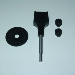May include: A black sanding tool with a metal shaft and a black sanding disc. The tool also includes two black rubber feet.