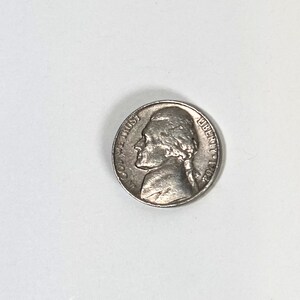 May include: A silver nickel coin featuring a profile of Thomas Jefferson. The coin has the words "IN GOD WE TRUST" and "LIBERTY" inscribed. The year 1962 is visible on the coin.