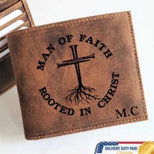 May include: Brown leather wallet with the text "MAN OF FAITH ROOTED IN CHRIST" and a cross design. The wallet is open, revealing card slots. The initials "M.C" are also visible.