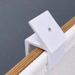 Può includere: Un morsetto a forma di C in plastica bianca con una piccola vite metallica centrata sulla superficie superiore. Il morsetto è fissato saldamente al bordo di una cornice in legno che sostiene un pezzo di tessuto bianco testurizzato.