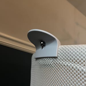K&ouml;nnte beinhalten: Nahaufnahme eines grauen Netz-Kinderbett-Einsatzes mit einem grauen Kunststoff-Anbauteil. Das Anbauteil hat eine kleine silberne Schraube in der Mitte.