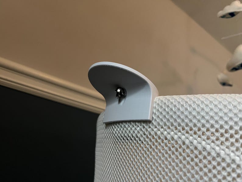 K&ouml;nnte beinhalten: Nahaufnahme eines grauen Netz-Kinderbett-Einsatzes mit einem grauen Kunststoff-Anbauteil. Das Anbauteil hat eine kleine silberne Schraube in der Mitte.