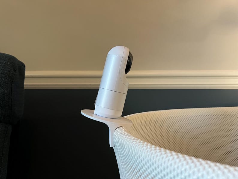 K&ouml;nnte beinhalten: Wei&szlig;er Babymonitor mit einer Kameraobjektiv, das auf einem wei&szlig;en St&auml;nder montiert ist. Der Monitor ist auf einem wei&szlig;en Stubenwagen positioniert.