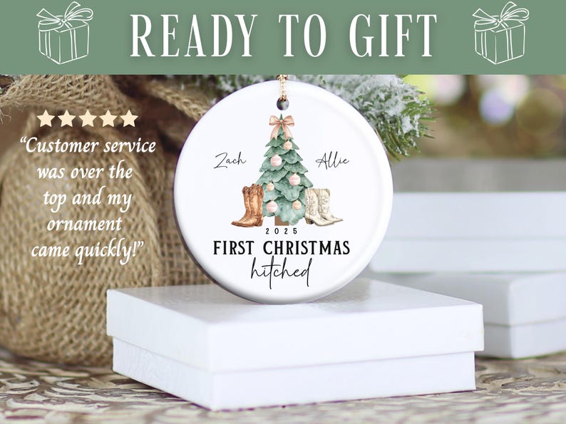 Op de afbeelding: Witte keramische kerstversiering met een boom, cowboylaarzen en de tekst "First Christmas hitched". De namen "Zach" en "Allie" staan boven de laarzen. De versiering ligt op een witte doos.